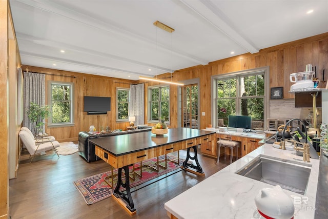 kitchen with beamed ceiling, wooden walls, dark wood-type flooring, and sink