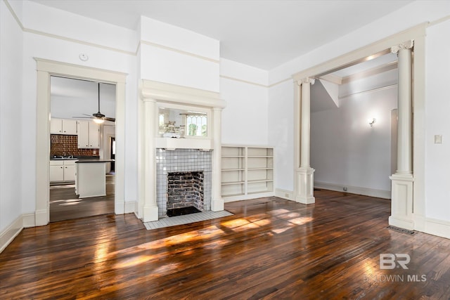 unfurnished living room with dark wood-type flooring, a fireplace, decorative columns, and ceiling fan