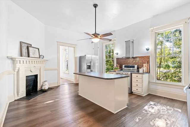 kitchen with plenty of natural light, stainless steel appliances, dark hardwood / wood-style flooring, and wall chimney range hood