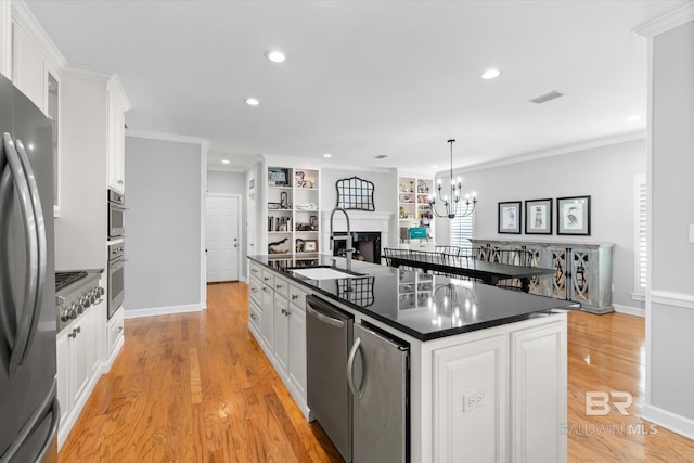 kitchen with a center island with sink, crown molding, decorative light fixtures, light hardwood / wood-style floors, and white cabinetry