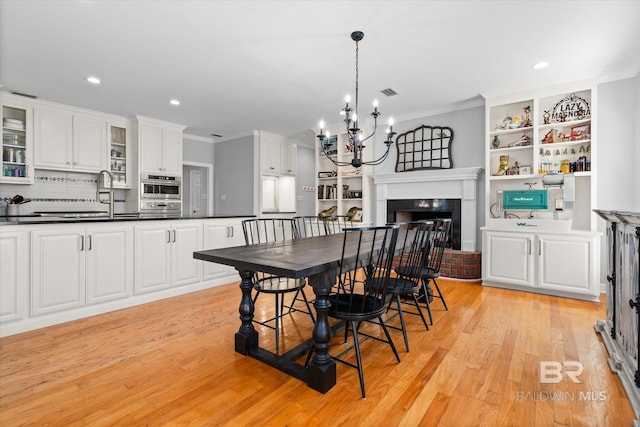 dining room featuring a notable chandelier, light hardwood / wood-style floors, ornamental molding, and sink