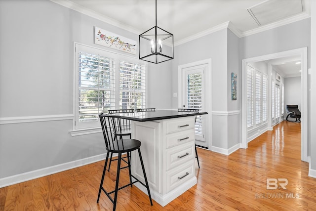 kitchen featuring hanging light fixtures, light hardwood / wood-style flooring, ornamental molding, a kitchen bar, and white cabinetry