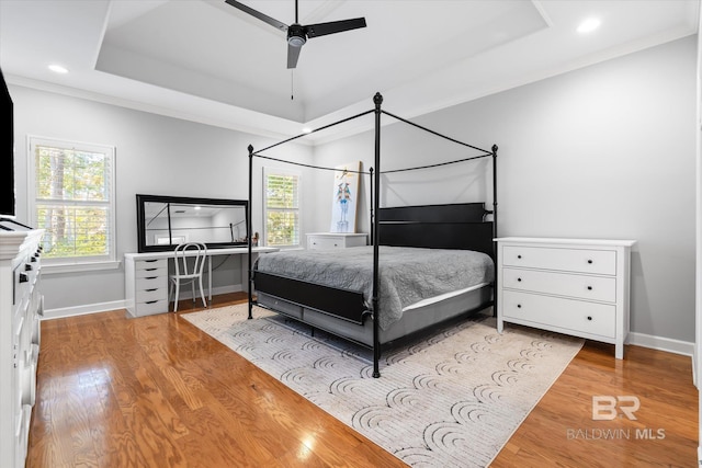 bedroom with ornamental molding, light hardwood / wood-style floors, ceiling fan, and a tray ceiling