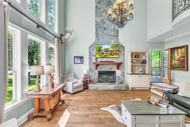 living area with a stone fireplace, a high ceiling, wood finished floors, and a notable chandelier