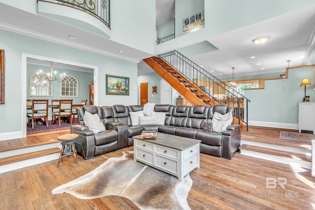 living room featuring light wood finished floors, an inviting chandelier, stairs, and crown molding