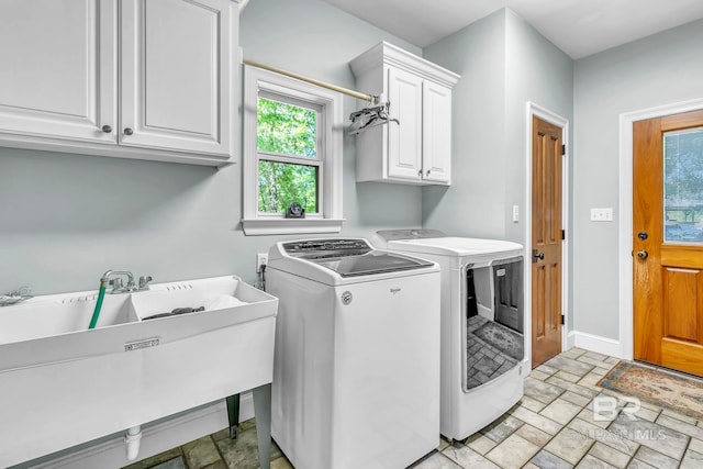 washroom with washing machine and clothes dryer, a sink, baseboards, stone finish flooring, and cabinet space