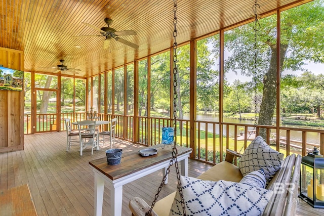 sunroom with ceiling fan, a healthy amount of sunlight, outdoor dining area, and a water view