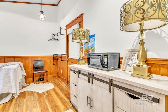interior space featuring wood walls, crown molding, a wainscoted wall, and light wood-type flooring