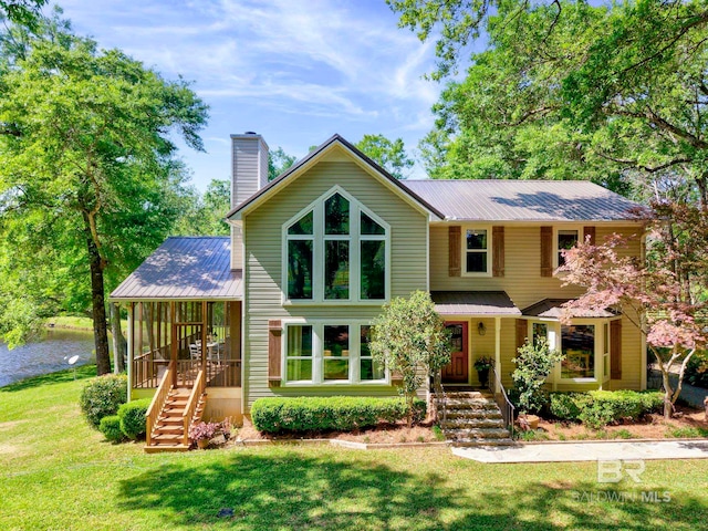 view of front of home with a front lawn, a sunroom, a chimney, and metal roof