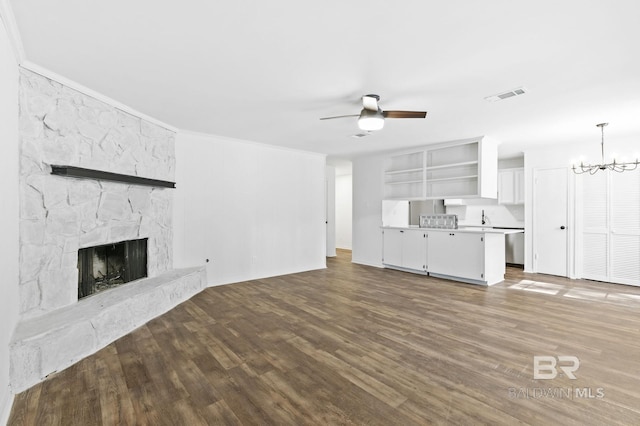 unfurnished living room featuring hardwood / wood-style flooring, built in shelves, crown molding, ceiling fan with notable chandelier, and a stone fireplace