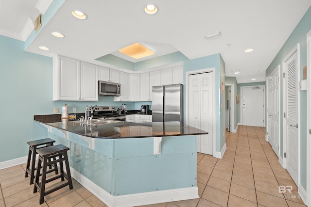 kitchen featuring light tile patterned floors, a kitchen breakfast bar, white cabinets, kitchen peninsula, and stainless steel appliances