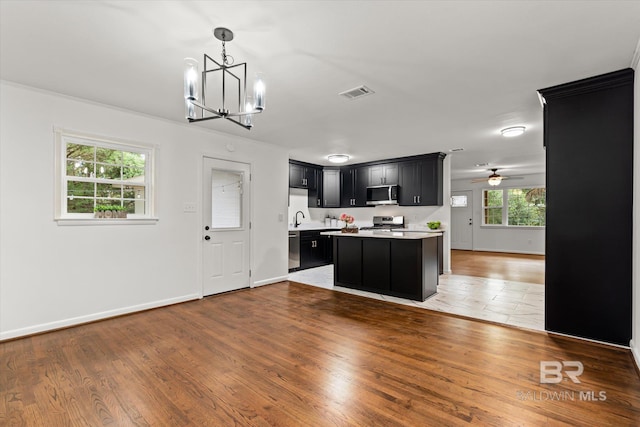 kitchen with a center island, decorative light fixtures, appliances with stainless steel finishes, ceiling fan with notable chandelier, and hardwood / wood-style flooring