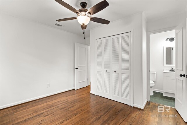 unfurnished bedroom with sink, ensuite bath, ceiling fan, dark hardwood / wood-style flooring, and a closet