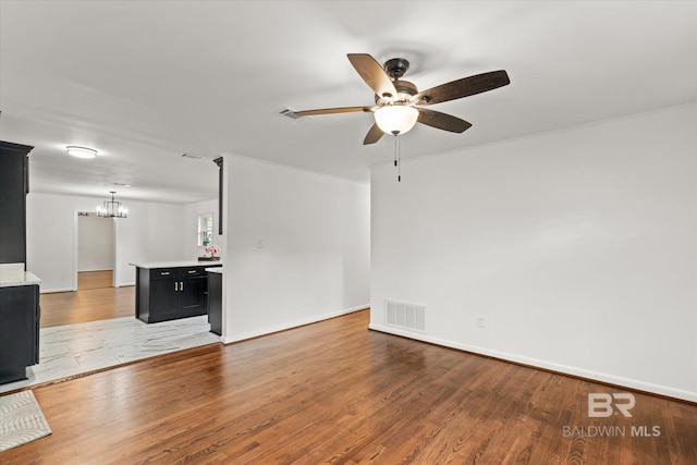 unfurnished living room featuring ceiling fan with notable chandelier and light wood-type flooring