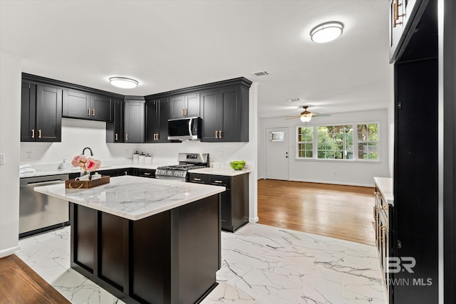 kitchen with light stone countertops, a center island, ceiling fan, light hardwood / wood-style flooring, and appliances with stainless steel finishes