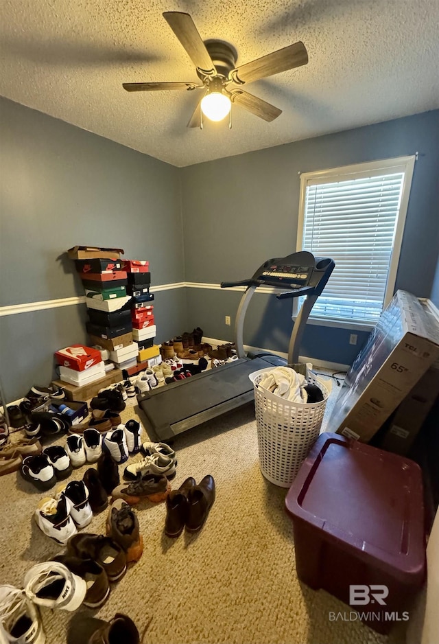 exercise room featuring ceiling fan, carpet floors, and a textured ceiling