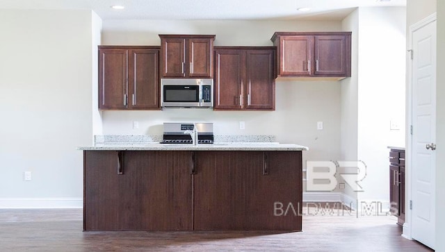 kitchen featuring light stone countertops, hardwood / wood-style floors, a breakfast bar, and sink