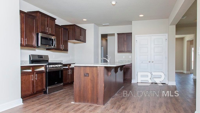 kitchen with dark hardwood / wood-style floors, stove, a kitchen island with sink, and a breakfast bar area