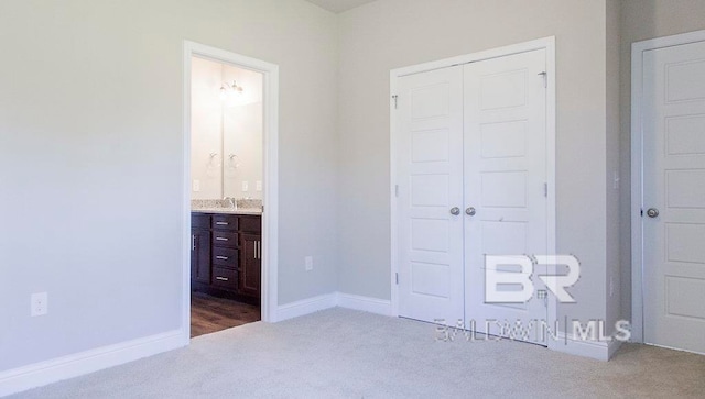 unfurnished bedroom with ensuite bathroom, sink, light carpet, and a closet