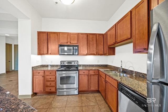 kitchen with sink, dark stone countertops, light tile flooring, and stainless steel appliances