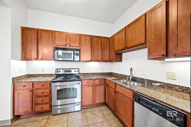 kitchen with sink, dark stone countertops, light tile flooring, and stainless steel appliances