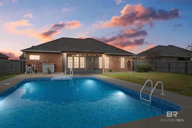 pool at dusk featuring a yard, an outdoor kitchen, and a patio area