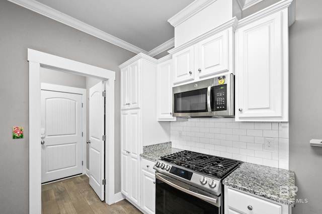 kitchen with appliances with stainless steel finishes, light stone counters, ornamental molding, hardwood / wood-style flooring, and white cabinetry