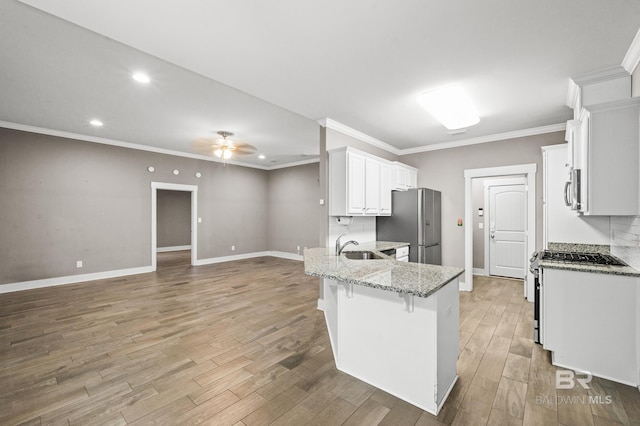 kitchen with a kitchen bar, stainless steel fridge, light stone counters, white range with gas cooktop, and white cabinetry