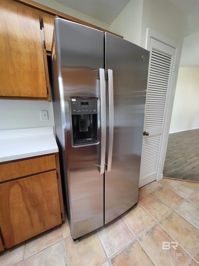kitchen featuring stainless steel fridge with ice dispenser, brown cabinets, light countertops, and light stone finish flooring