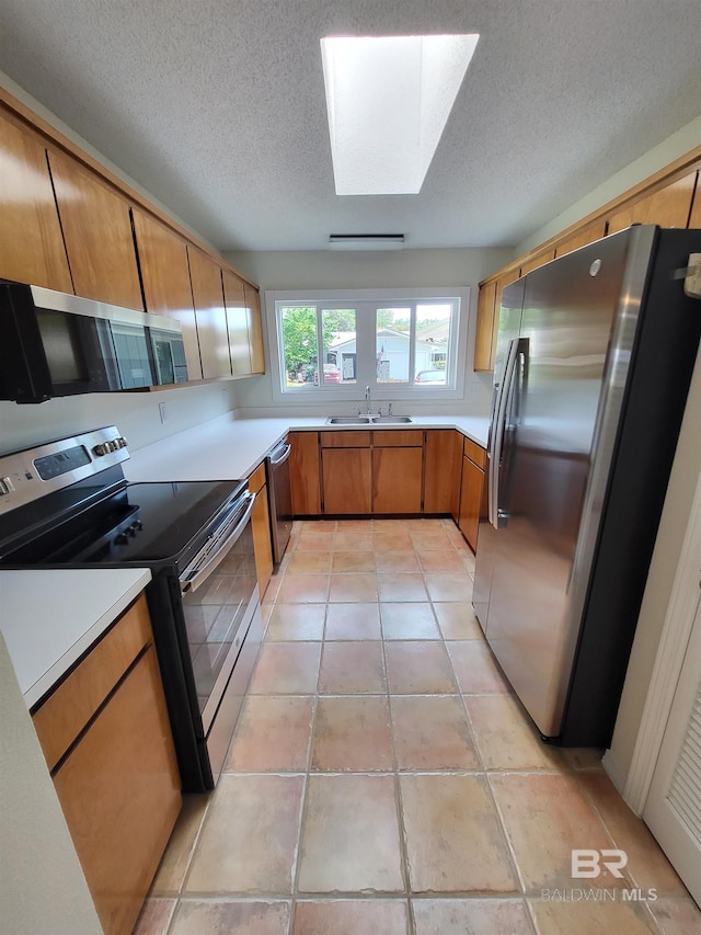 kitchen featuring stainless steel appliances, a skylight, brown cabinets, a sink, and light countertops