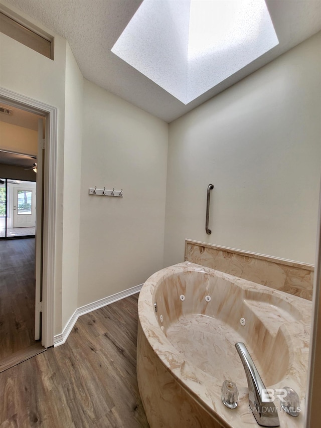 bathroom with a skylight, wood finished floors, a tub with jets, and baseboards