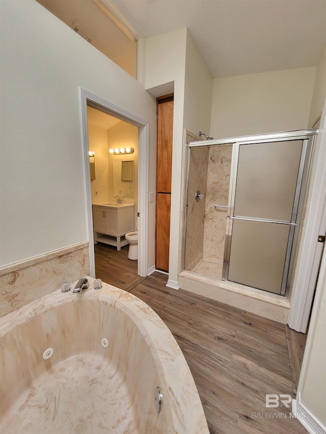 full bathroom featuring wood finished floors, a sink, a stall shower, a tub with jets, and toilet