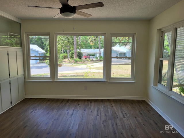 empty room featuring dark wood-style flooring, healthy amount of natural light, a ceiling fan, a textured ceiling, and baseboards