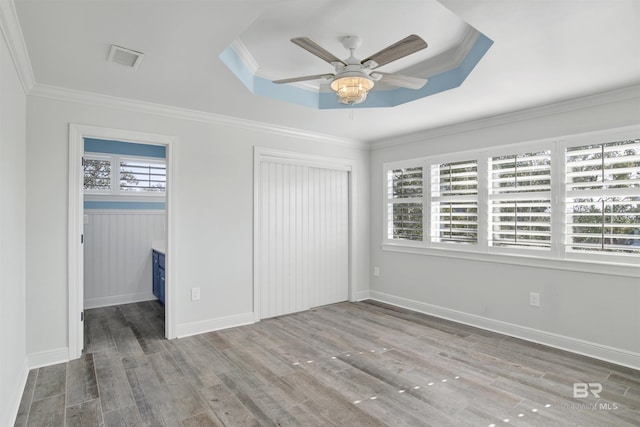 unfurnished bedroom with a walk in closet, hardwood / wood-style flooring, ceiling fan, ornamental molding, and a tray ceiling