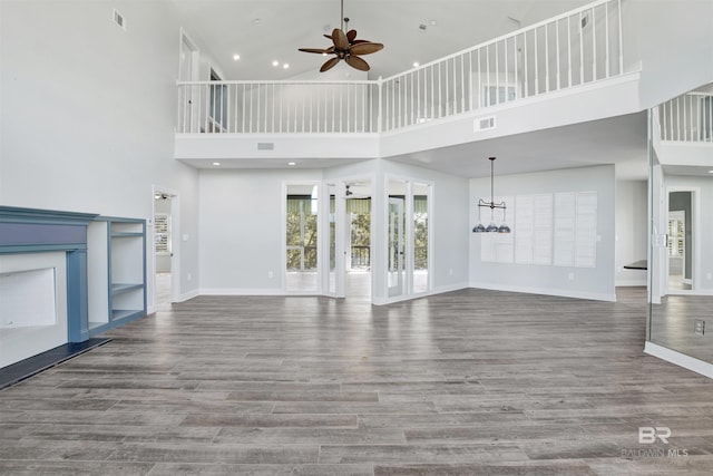 unfurnished living room with ceiling fan with notable chandelier, wood-type flooring, and a high ceiling