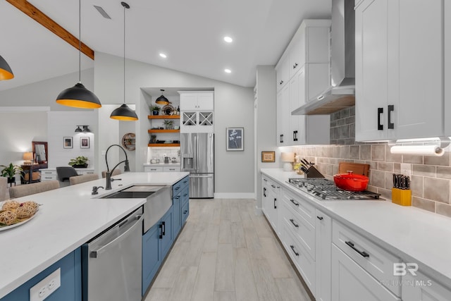 kitchen with wall chimney range hood, blue cabinets, appliances with stainless steel finishes, a sink, and white cabinets