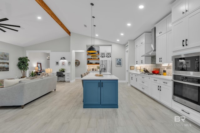 kitchen with open floor plan, wall chimney range hood, light countertops, white cabinets, and stainless steel appliances