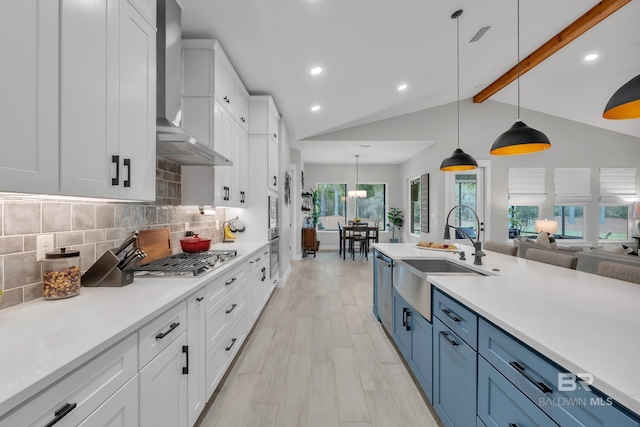 kitchen featuring appliances with stainless steel finishes, white cabinetry, a sink, lofted ceiling with beams, and wall chimney exhaust hood