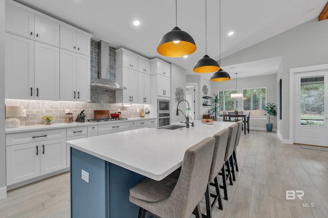 kitchen with appliances with stainless steel finishes, a sink, wall chimney exhaust hood, tasteful backsplash, and vaulted ceiling