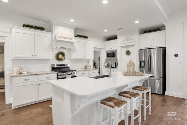 kitchen with crown molding, white cabinets, appliances with stainless steel finishes, a sink, and wood finished floors