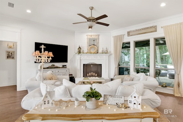 living area featuring visible vents, ornamental molding, wood finished floors, a fireplace with raised hearth, and a ceiling fan