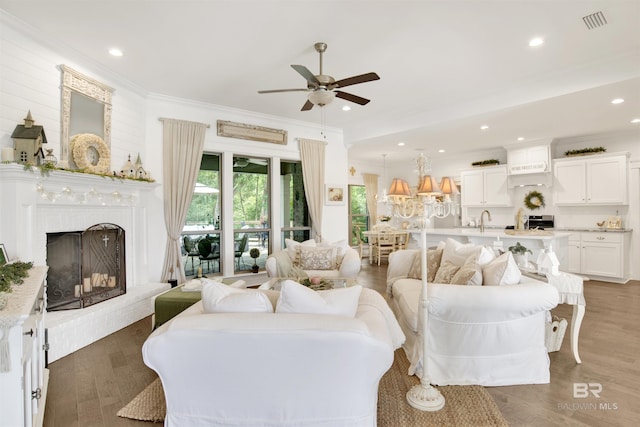 living area with ceiling fan, visible vents, a fireplace with raised hearth, ornamental molding, and recessed lighting