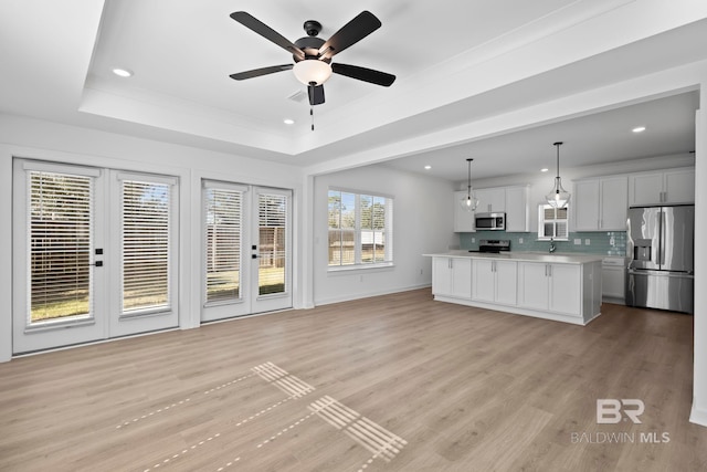 interior space with light wood finished floors, light countertops, decorative backsplash, appliances with stainless steel finishes, and a raised ceiling