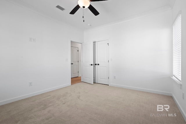 unfurnished bedroom with visible vents, ceiling fan, baseboards, light colored carpet, and ornamental molding