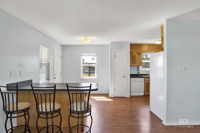 kitchen with dark wood finished floors, dark countertops, a breakfast bar, a peninsula, and white dishwasher