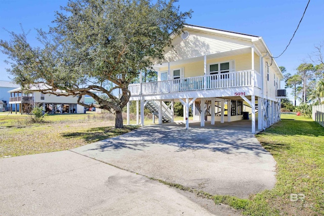 beach home with covered porch, a carport, driveway, a front lawn, and stairs