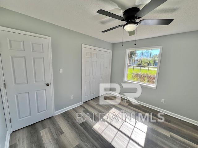 unfurnished room with a textured ceiling, ceiling fan, and dark wood-type flooring