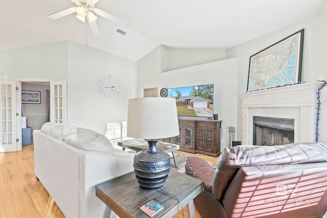 living room with high vaulted ceiling, french doors, light hardwood / wood-style flooring, ceiling fan, and a fireplace