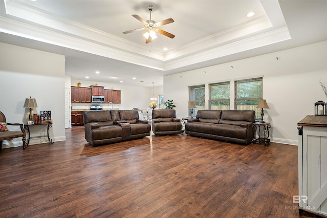 living room with ceiling fan, a raised ceiling, ornamental molding, and dark wood-type flooring