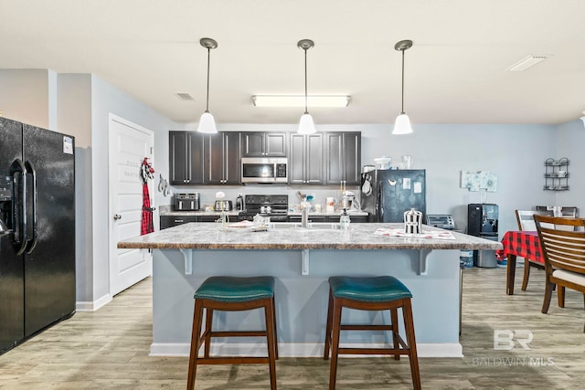 kitchen with black appliances, pendant lighting, light hardwood / wood-style floors, and a kitchen island with sink